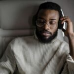 Home A man in a sweater enjoys music with headphones while sitting on an airplane.